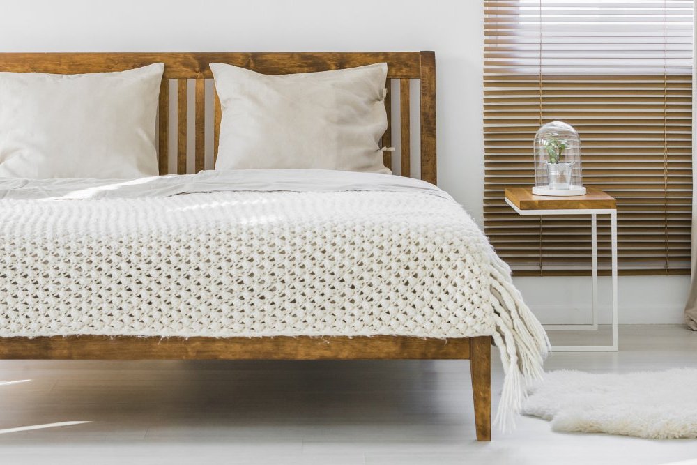 Drewniane podwójne łóżko z poduszkami i bocznym stolikiem